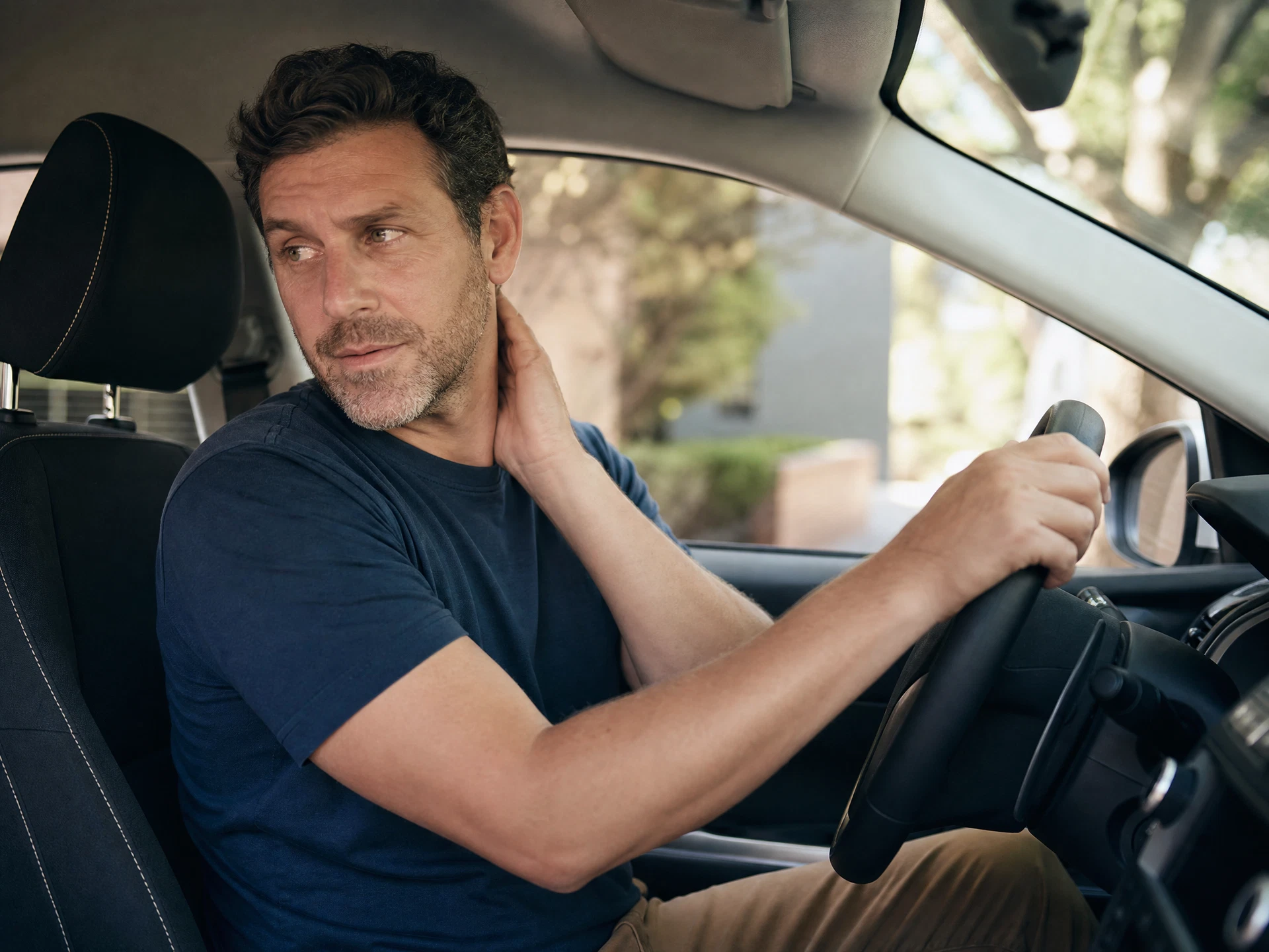 Man in car twisting to look over his shoulder while reversing, showing neck discomfort